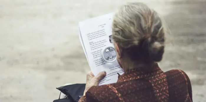 An elderley woman viewing a document with a magnifying glass to determine if she has a valid TPD claim